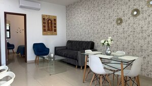 A modern living room with a grey sofa, a glass coffee table, and a dining area with white chairs and a marble table. - Rio Nilo Apartments (Mazatlán)