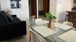 A modern living room with a glass dining table, a black sofa, and a decorative plant. - Rio Nilo Apartments (Mazatlán)