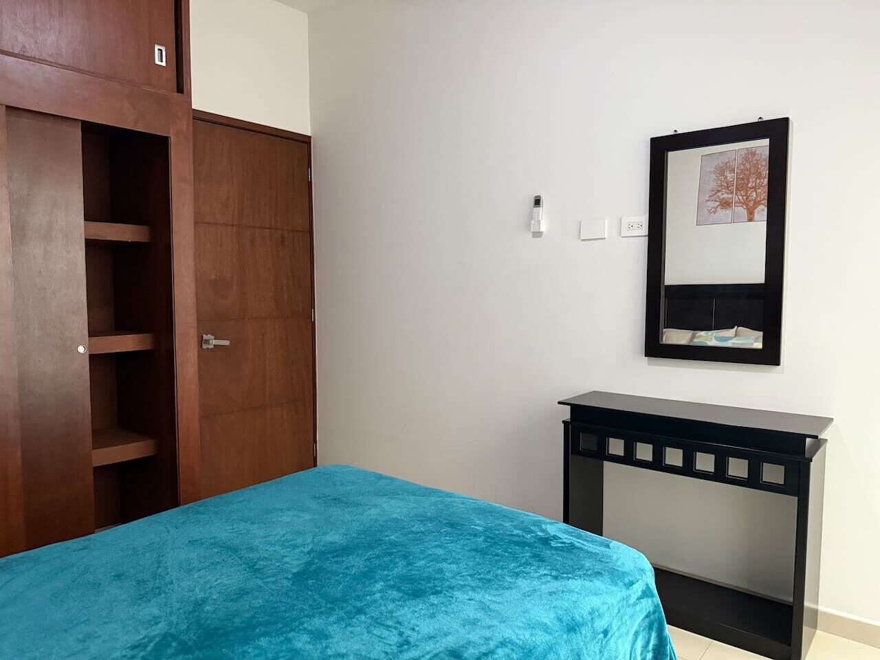 A bedroom with a bed, a wardrobe, a desk, and a framed picture on the wall.