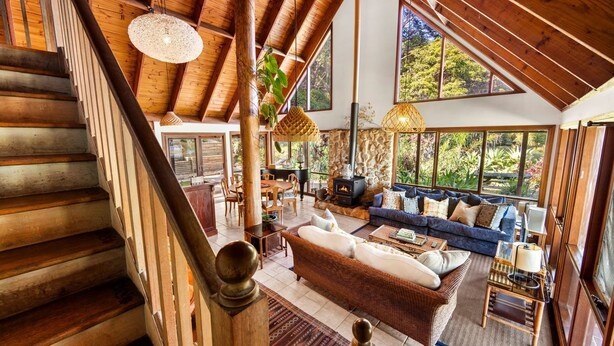 A spacious living area with a high ceiling, wooden staircase, and large windows offering views of the outdoors.