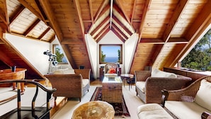 A cozy attic room with wooden beams, wicker furniture, and a view of the sea.