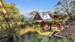 A modern house with a sloped roof, surrounded by lush greenery and a view of the ocean.
