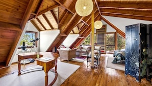 A spacious attic room with wooden beams, a telescope, wicker furniture, and a large window offering a view of the outdoors.