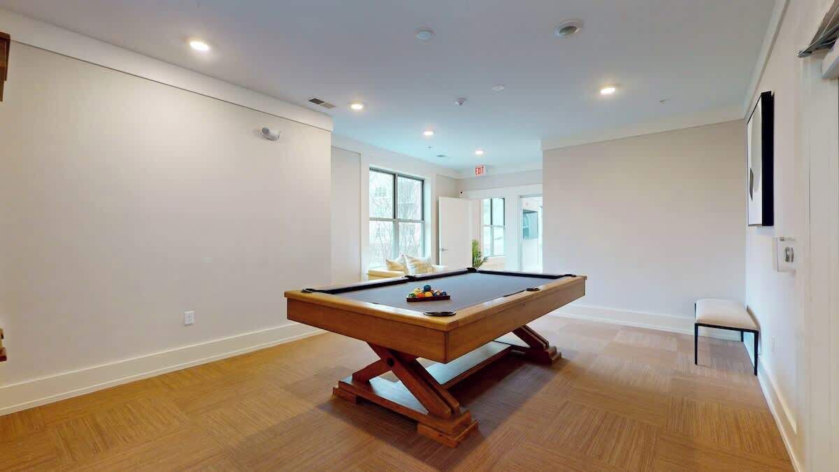 A pool table in a spacious room with wooden flooring and white walls.