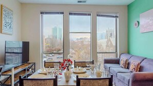 A modern living room with a dining area, large windows, a flat-screen TV, and a green accent wall. - Stylish Home With Free ParkingFA (Stamford)