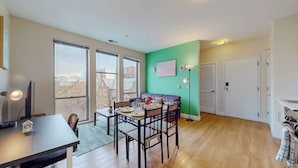 A dining area with a table set for four, a sofa, and a view of the city through large windows. - Stylish Home With Free ParkingFA (Stamford)