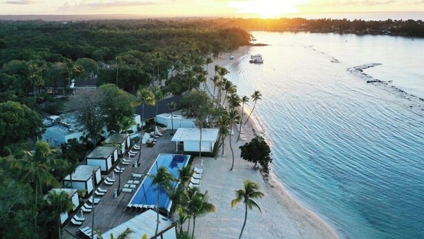 Vista aérea de un resort con playa, área de piscina y un barco en el agua.