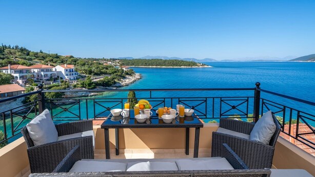 Un balcon agrémenté de meubles en osier, une table mise pour le petit-déjeuner et une vue sur la mer et la côte.