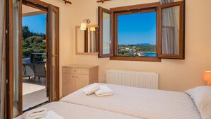 Une chambre à coucher comprenant un lit, une table de chevet, une commode et une fenêtre donnant sur la ville et les collines.