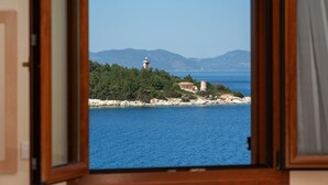 Une vue sur la côte, aperçue à travers une fenêtre, avec un phare, une côte rocheuse et des montagnes au loin.