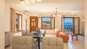 Un vaste espace de vie comprenant une table à manger, des sièges confortables et une vue sur la mer grâce à de grandes fenêtres.