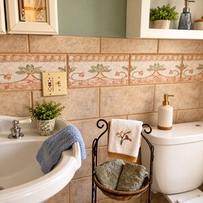 Une salle de bain équipée d’une baignoire, de toilettes, d’un lavabo, d’un porte-serviettes, d’une plante en pot et d’un distributeur de savon.