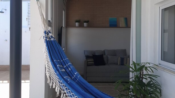 Uma rede em um quarto com um sofá cinza, uma planta em vaso e uma parede de tijolos.