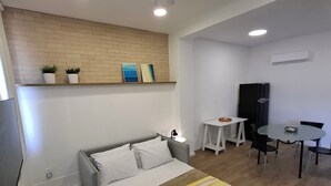 Quarto de hotel moderno com cama, mesa de cabeceira e pequena escrivaninha com cadeiras.