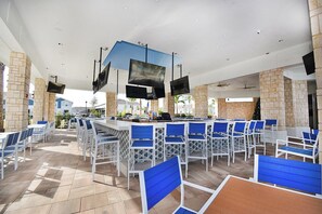 An outdoor bar area with multiple seating arrangements, including bar stools and tables, and a counter with a television screen. - Windsor Island Pool Home | Private Pool & BBQ | Lazy River Resort | Near Disney (Davenport)