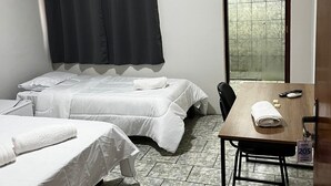 Ein Hotelzimmer mit zwei Betten, einem Tisch mit Fernbedienung, einem Handtuch und einem Fenster mit Blick.