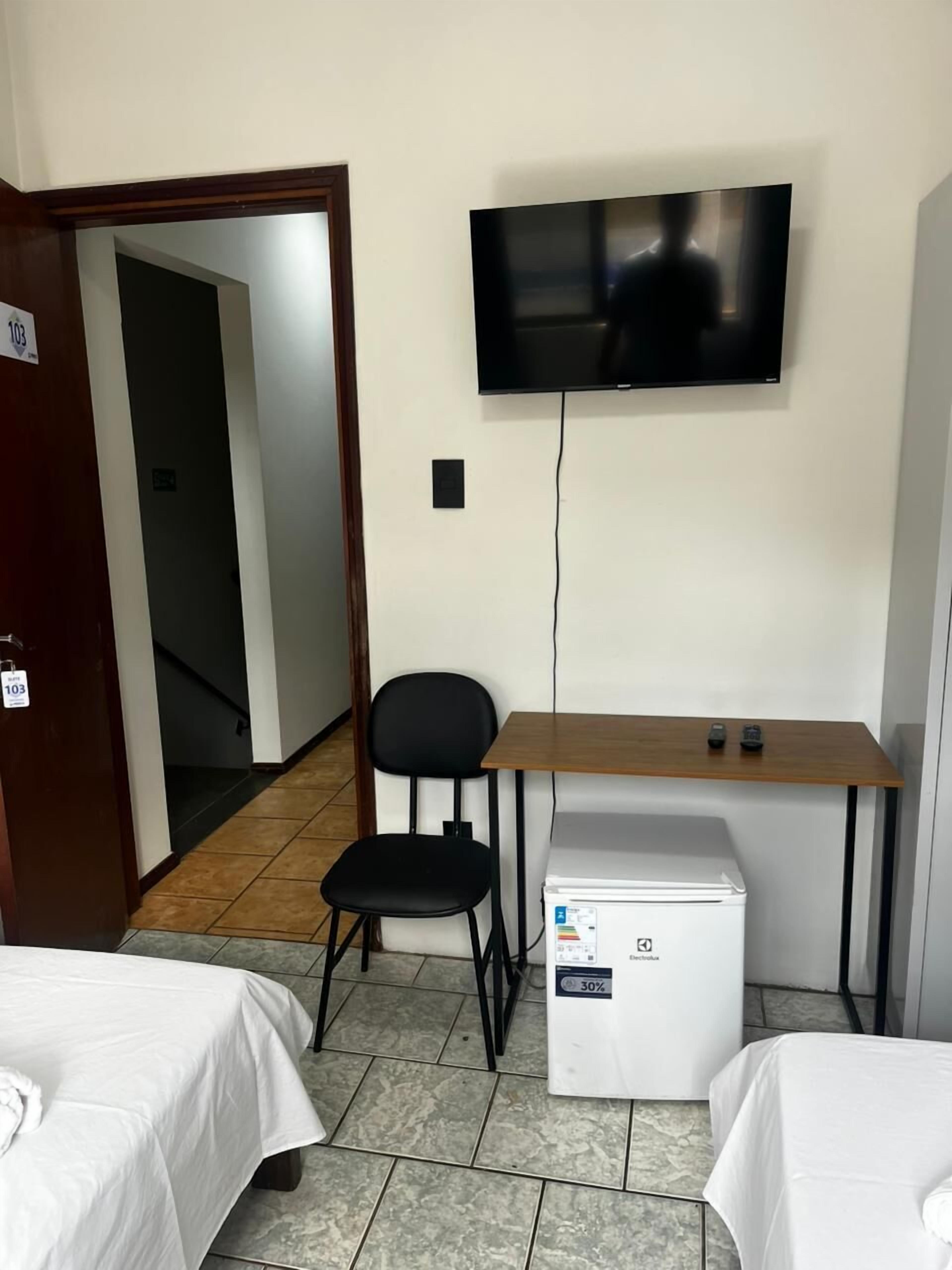 A hotel room with a bed, a desk with a chair, a television, and a refrigerator.