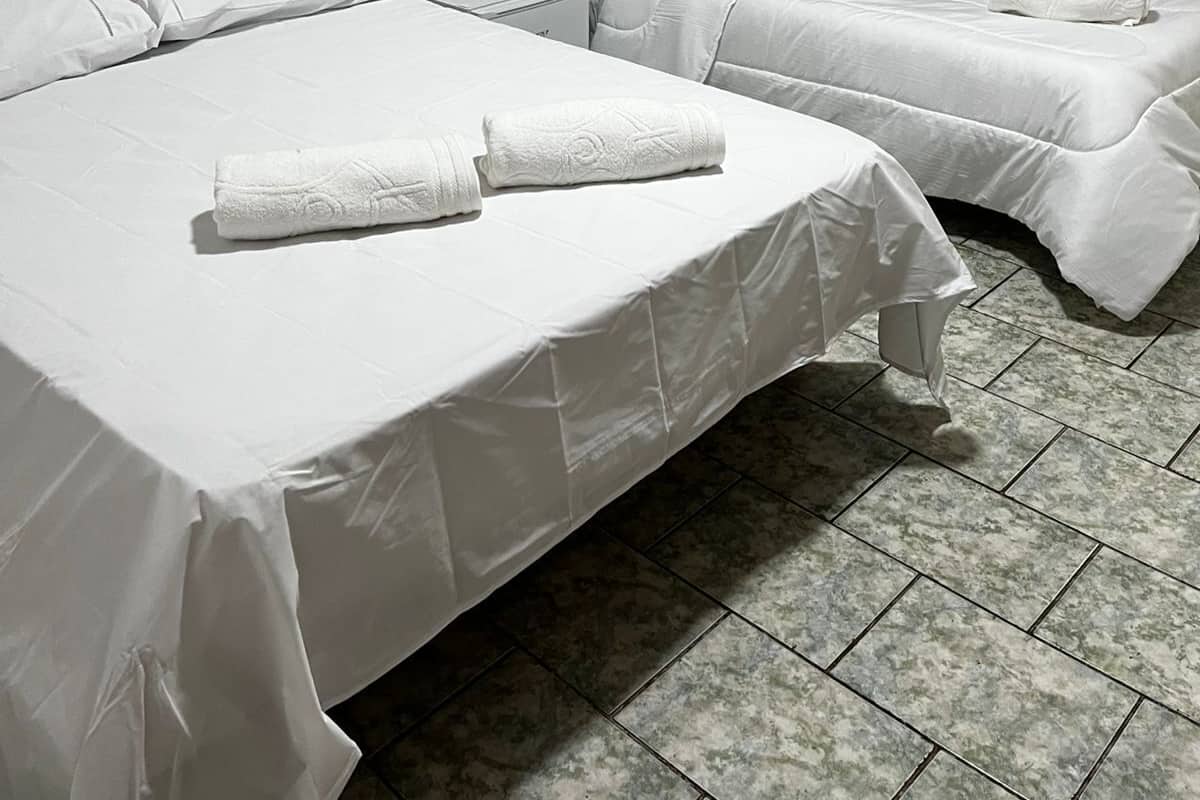 A hotel room with two single beds, a small table, a nightstand, and a window with dark curtains.