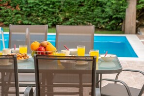 Ein Frühstücksbuffet mit Früchten, Saft und Müsli an einem Pool mit Stühlen und einem Tisch.