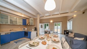 Een moderne keuken met blauwe kastjes, een eethoek met een tafel voor vier personen, en een grijze bank in de woonkamer.