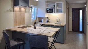 A compact kitchen with a built-in microwave, a sink, and a small dining area with two chairs. - Lovely apartment in Kraljevica with WiFi (Kraljevica)