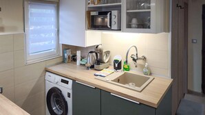 A compact kitchen with a washing machine, a microwave, a sink, and a window with blinds. - Lovely apartment in Kraljevica with WiFi (Kraljevica)