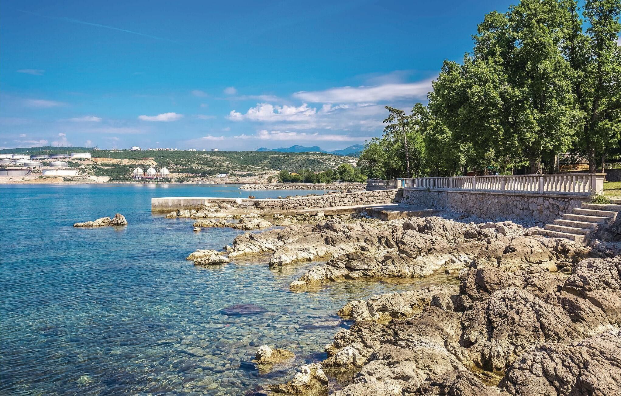 A coastal area with clear waters, rocky terrain, and a stone staircase leading to a viewing platform.