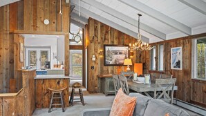 Een rustiek interieur met houten wanden, een eethoek en een woonkamer met een grijze bank en oranje kussens.