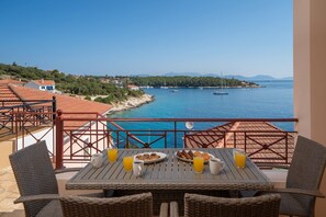 A balcony with a table set for breakfast overlooking a coastal view with boats and hills. - Beachfront Aetheria House, Wonderful Sea Views, Furnished Terrace, Fiskardo (Kefalonia)