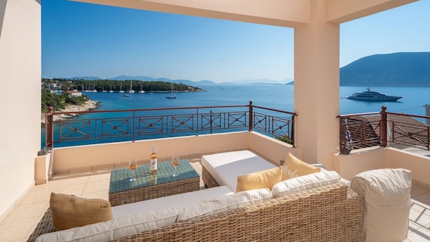 A balcony with a view of a calm sea and boats, furnished with a sofa and a table with a bottle and glass. - Beachfront Aetheria House, Wonderful Sea Views, Furnished Terrace, Fiskardo (Kefalonia)