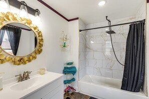 Een badkamer met een witte wastafel, spiegel met gouden lijst en een douche met een zwart gordijn.