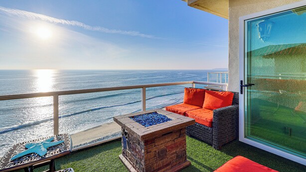 Un balcon avec vue sur l’océan, un foyer extérieur et du mobilier de jardin.