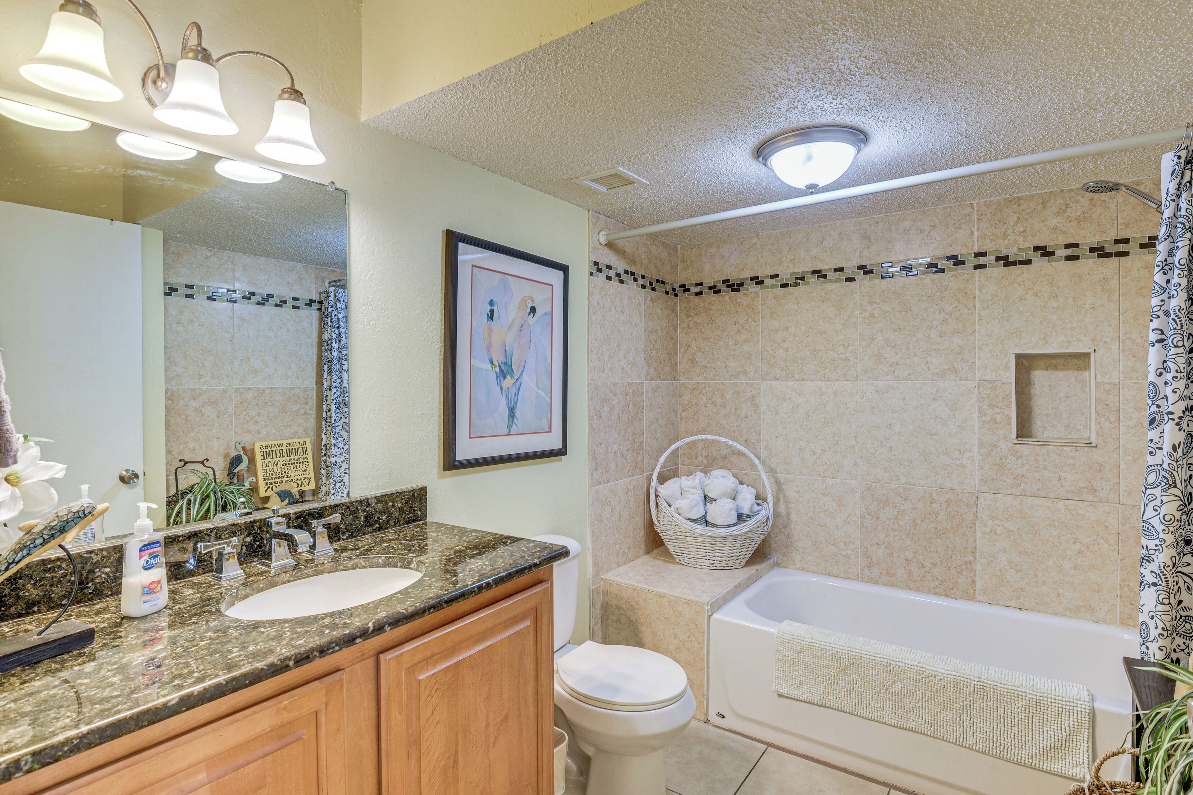 A bathroom with a sink, toilet, and bathtub, featuring a mosaic tile shower area and a framed artwork on the wall.