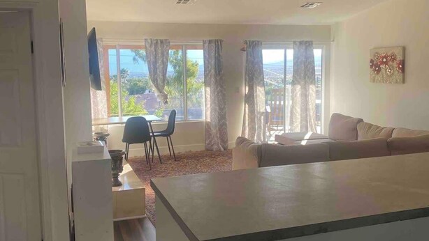 Ein modernes Wohnzimmer mit Sofa, Essbereich mit Tisch und Stühlen sowie ein großes Fenster mit Vorhängen.