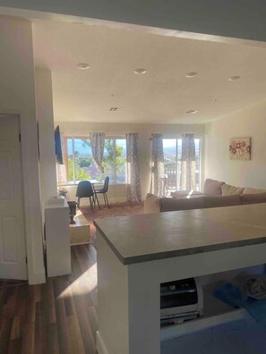 A modern living room with a sofa, a dining area with a table and chairs, and a large window with curtains.