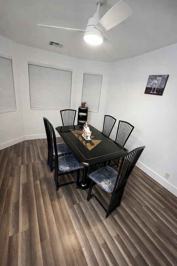 A dining area with a black table, six chairs, and a ceiling fan.
