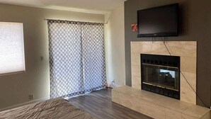 Ein Wohnzimmer mit Kamin, einem an der Wand montierten Fernseher und einem gemusterten Vorhang.