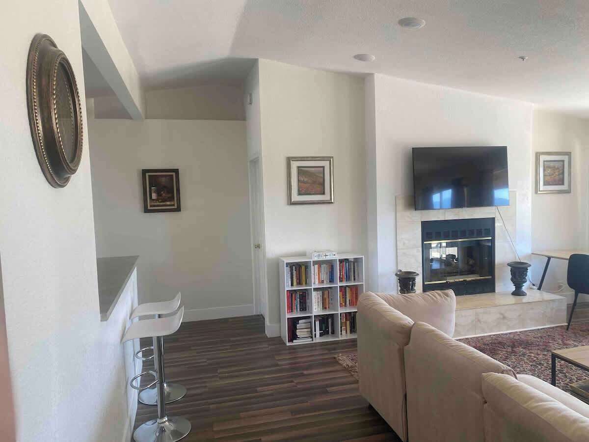 A living room with a sofa, bookshelf, flat-screen TV, fireplace, and a dining area.