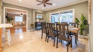 A dining area with a wooden table and chairs, a ceiling fan, and a large window. - Marbella Lane - Charming 4BR Bungalo for Relaxing Retreat (Fullerton)