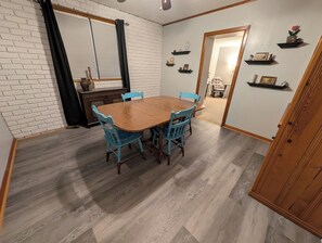 Een eetgedeelte met een houten tafel en blauwe stoelen, een witte bakstenen muur en een houten vloer.