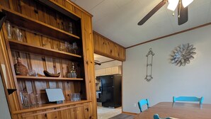 Ein Essbereich mit Holztisch und -stühlen, einem Deckenventilator und einer Holzkommode mit Gläsern.