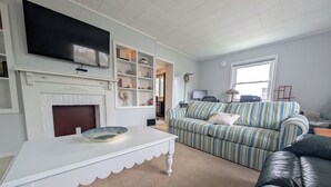 Ein Wohnzimmer mit Kamin, einem gestreiften Sofa, einem schwarzen Ledersessel und einem Fernseher an der Wand.