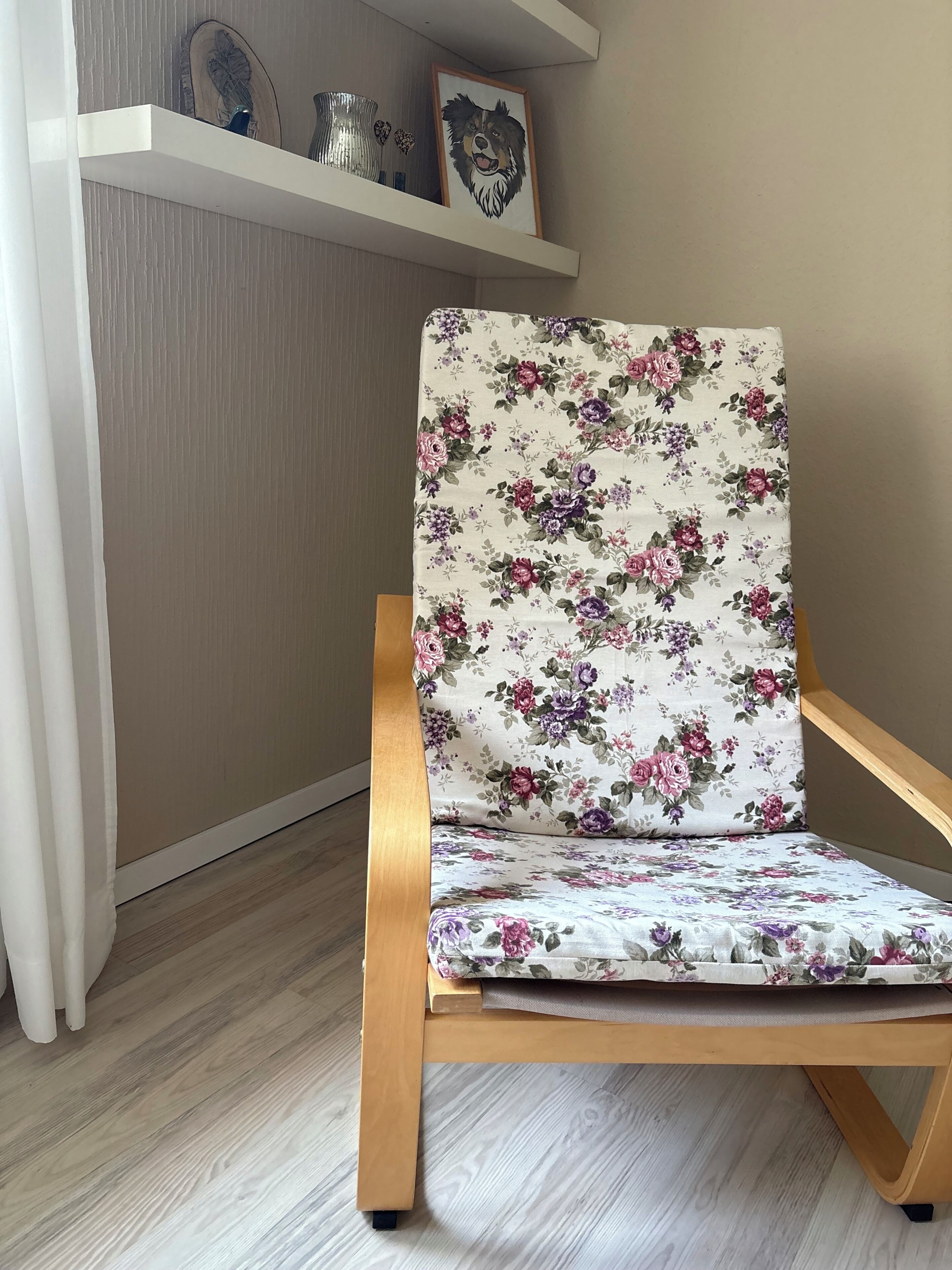 A wooden-framed chair with a floral-patterned cushion, positioned in a room with a wooden floor and a white wall.