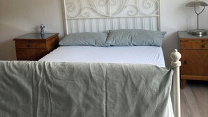 A bed with a white headboard, a grey bedspread, a wooden nightstand with a lamp, and a wall-mounted decoration.