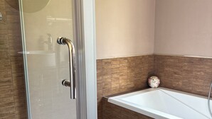 A bathroom with a glass shower enclosure, a white bathtub, and wooden wall tiles.