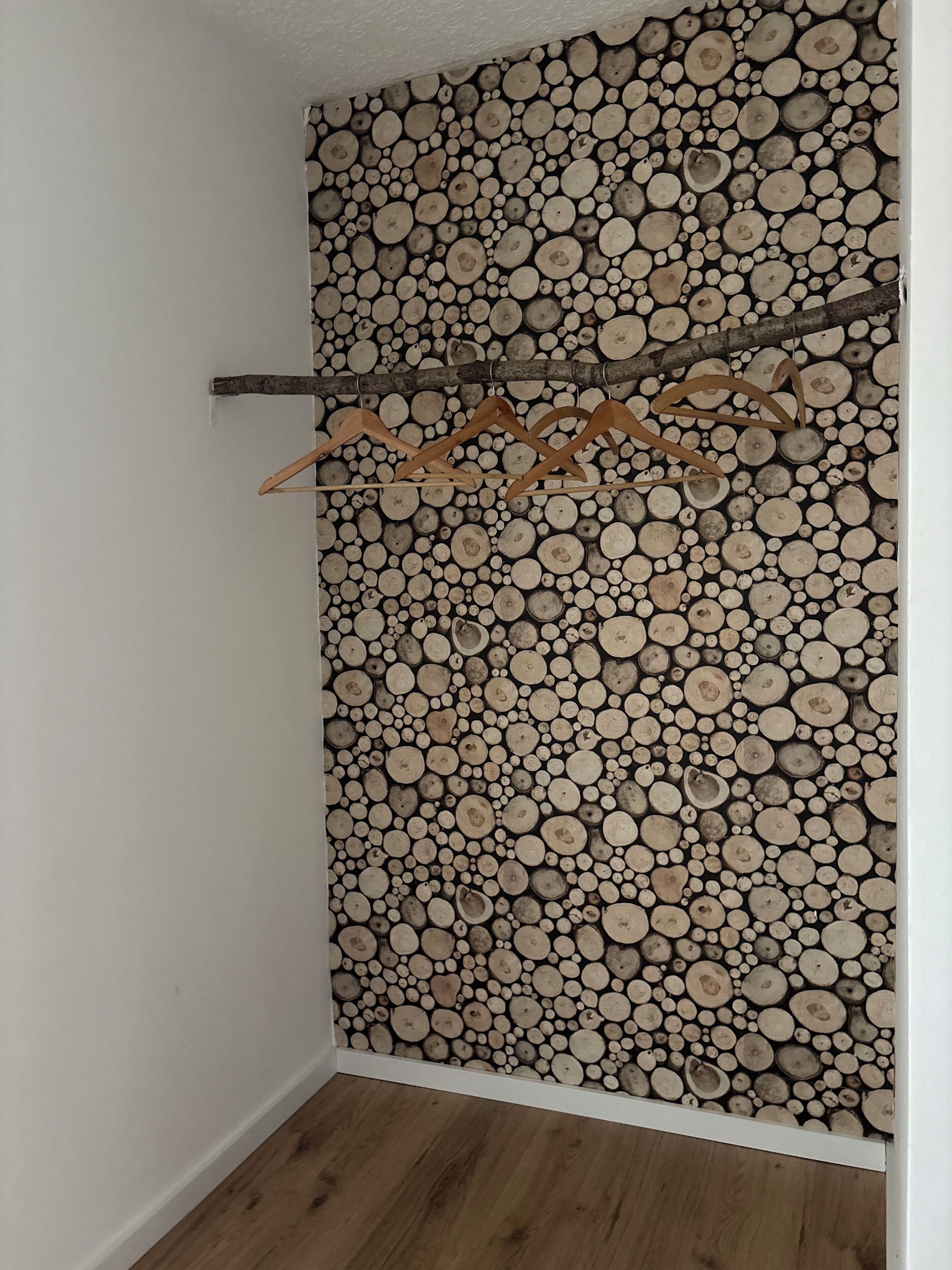Una stanza con un muro ricoperto di legna impilata, un appendiabiti in legno e pavimento di legno.