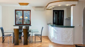 A modern kitchen with a curved island, a dining area with a glass table and chairs, and a built-in air conditioning unit. - Gorgeous apartment in Opric with house sea view (Opric)