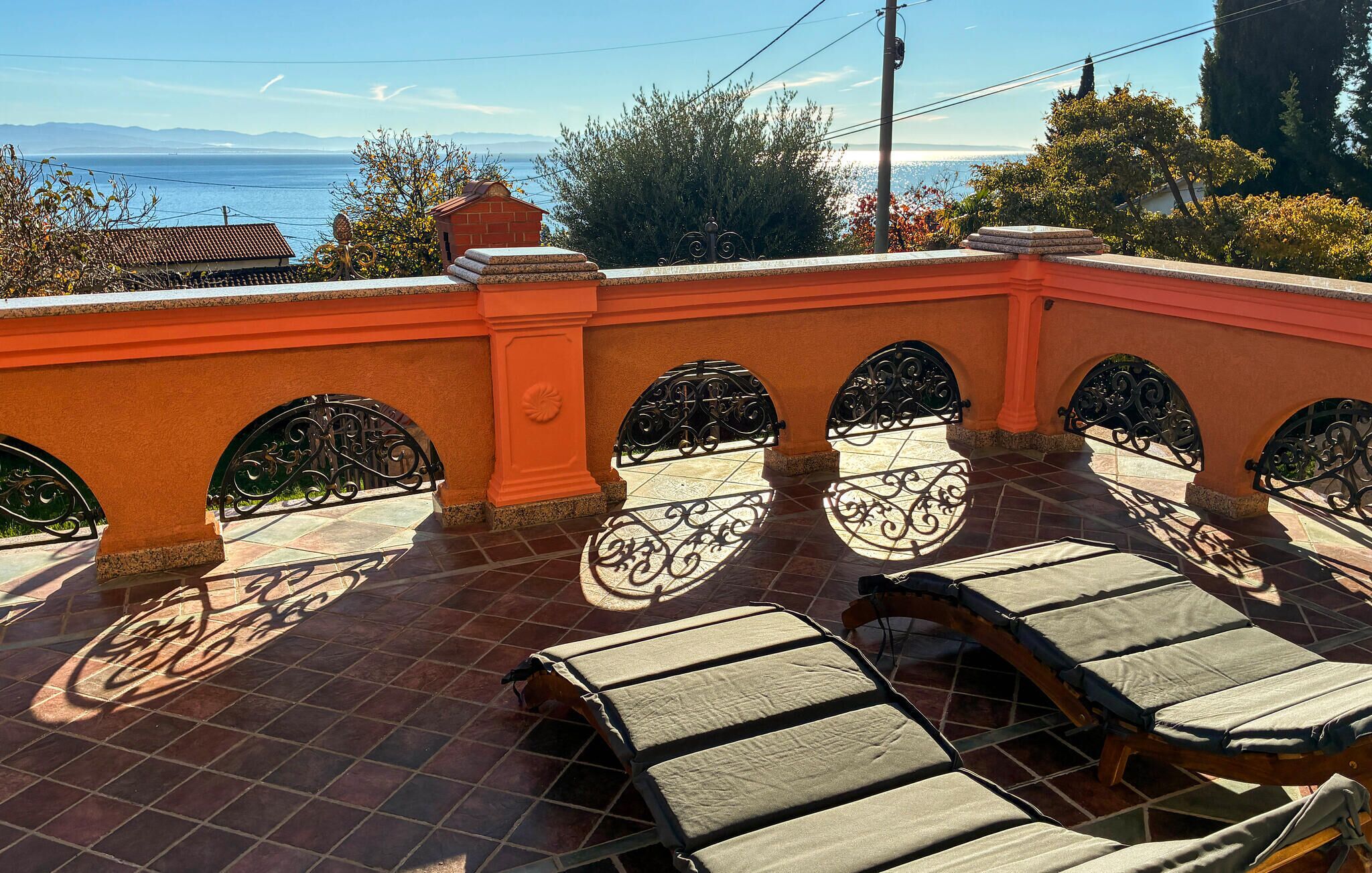 A terrace with a view of the sea, featuring a tiled floor and a row of sun loungers.