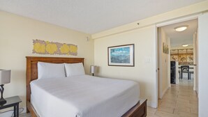 A hotel room with a bed, a nightstand, a lamp, a framed picture on the wall, and a view into the dining area. - High-Floor Waikiki Apt w/ Views & Pool (Honolulu)