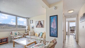 A spacious living room with a large window, wicker furniture, and a view of the city. - High-Floor Waikiki Apt w/ Views & Pool (Honolulu)